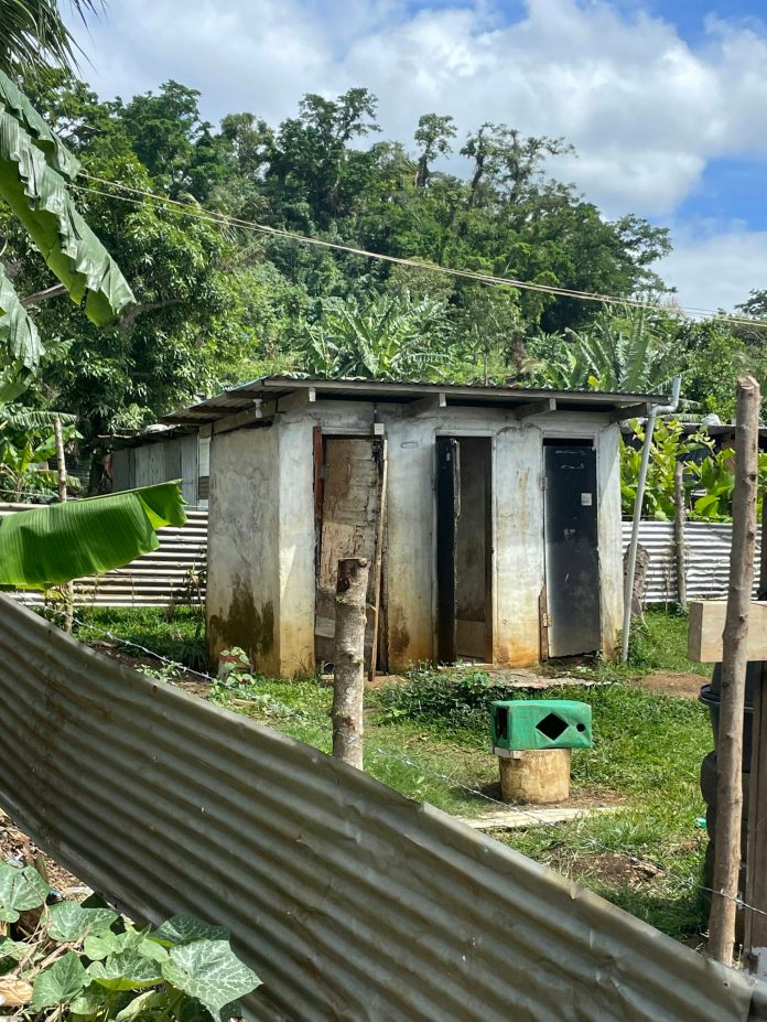 A toilet block outdoors with mountain and trees behind.