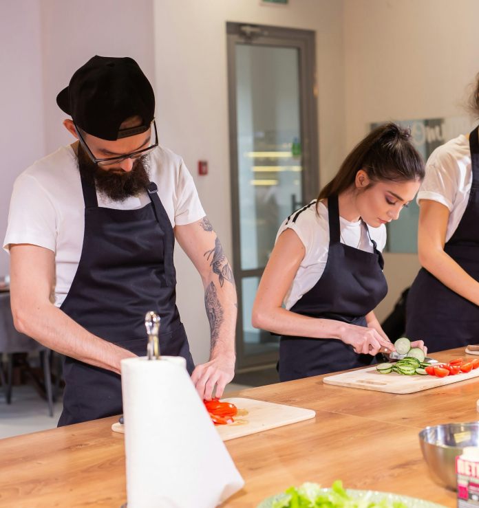 Cooking course where a senior male chef in uniform teaches young people to slice vegetables